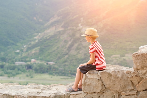 Niño con sombrero sentado sobre piedras