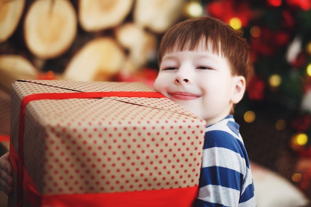 Niño con sombreros de Navidad está sentado con cajas de regalo en sus manos con la alegría de una sorpresa.