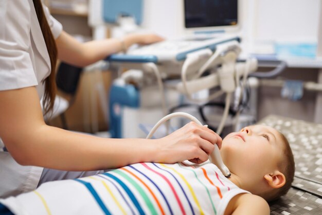 Niño sometido a un examen de ultrasonido de la tiroides Médico examinando la garganta del niño en la clínica con equipo