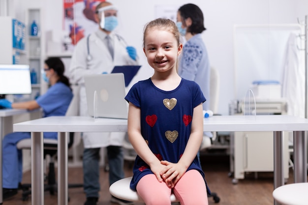 Niño sonriendo a la cámara durante el examen médico en la oficina del hospital. Especialista en medicina brindando servicios asistenciales de consulta, tratamiento radiográfico en clínica.