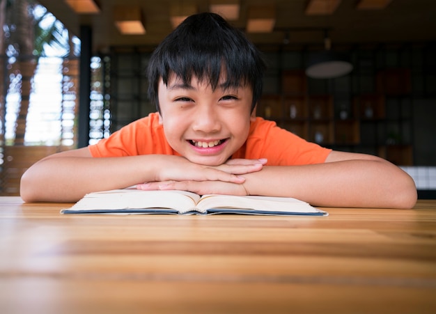 Niño sonriendo con un libro sobre la mesa de madera. Aprendiendo en casa