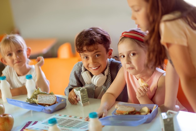 Niño sonriendo mientras está sentado cerca de las niñas almorzando juntos