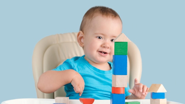 Un niño sonriente de entre 12 y 17 meses se regocija en una casa construida por sí mismo con cubos de madera. Juegos infantiles educativos para recién nacidos.