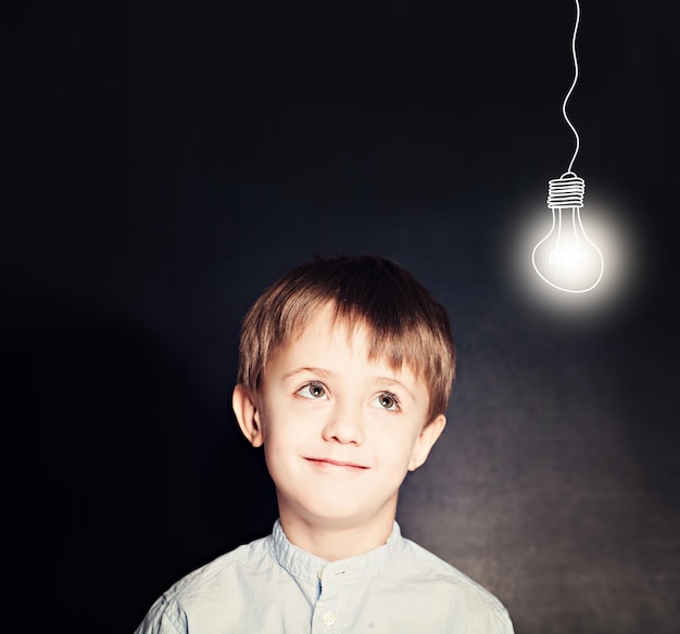 Niño sonriente alegre con bombilla en la pizarra. Ideas y concepto de escuela