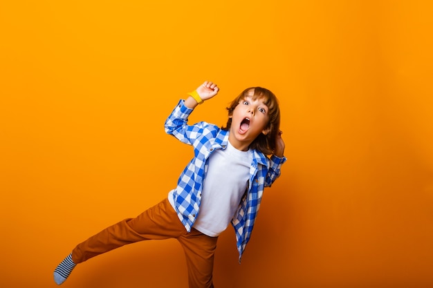 Niño sonriente alegre saltando y divirtiéndose en la pared amarilla. Concepto de escuela.