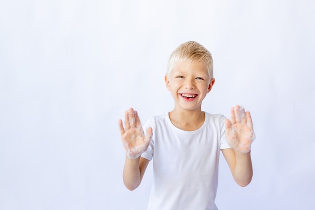 Foto niño sonriente con una camiseta blanca muestra sus manos en espuma