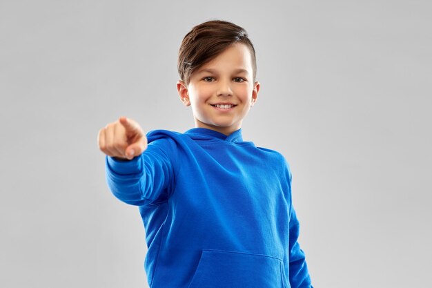 Foto niño sonriente con capucha azul señalando con el dedo