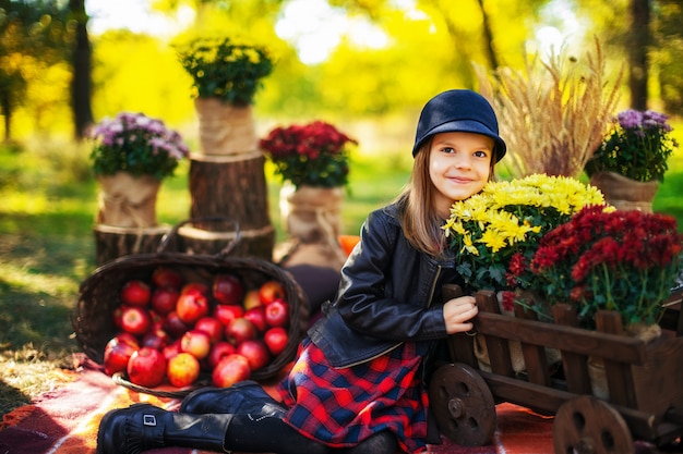 Niño sonriente con una cesta de manzanas rojas sentado en el parque otoño