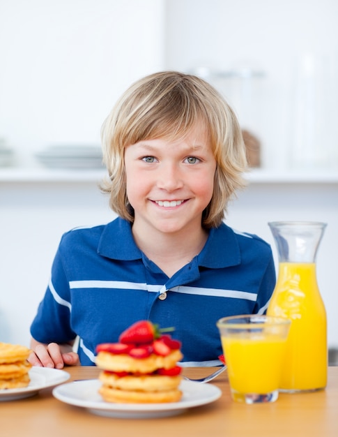 Niño sonriente comiendo waffles con fresas