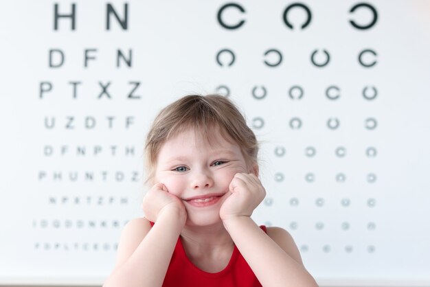 Niño sonriente contra la mesa de prueba de visión en retrato de clínica médica