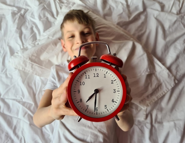 Niño sonriente con un despertador en la cama