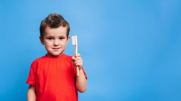 Un niño sonriente con dientes sanos sostiene un cepillo de dientes sobre un fondo azul aislado Higiene oral Un lugar para su texto