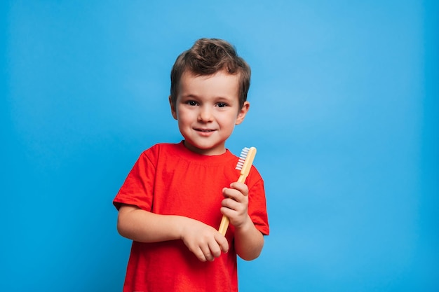 Un niño sonriente con dientes sanos sostiene un cepillo de dientes sobre un fondo azul aislado Higiene oral