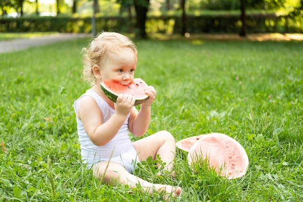 niño sonriente divertido en traje blanco comiendo sandía en el césped verde