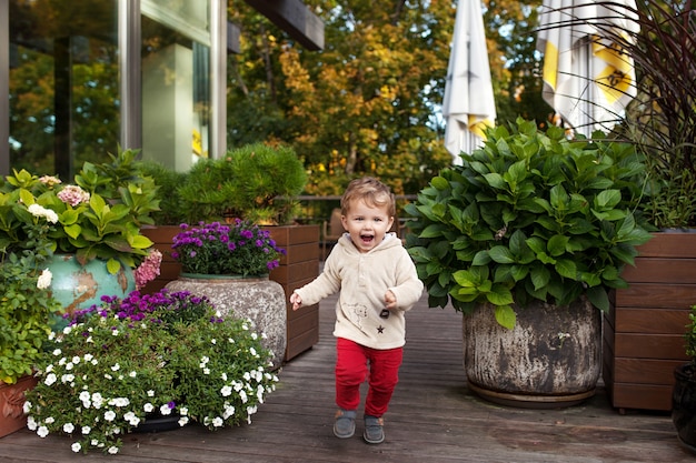 Niño sonriente se ejecuta en una terassa de café. Niño encantador sonríe y tiene alegría. Actividades al aire libre para niños