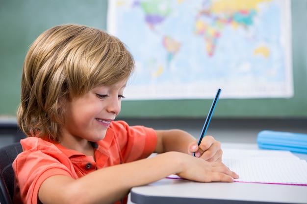 Niño sonriente escribiendo en el libro en el aula