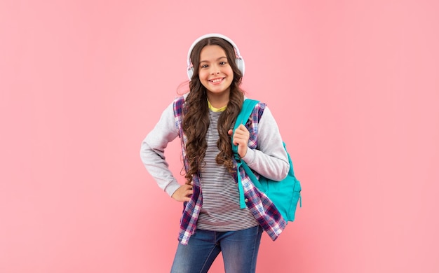 Niño sonriente escucha música en auriculares y lleva mochila en la infancia de fondo rosa