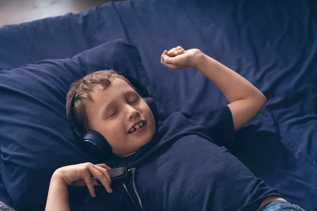Niño sonriente escuchando música con auriculares, acostado en la cama