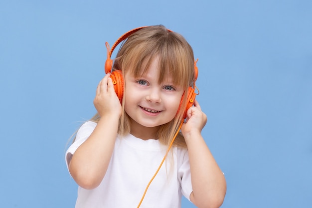 Niño sonriente feliz disfruta escucha música en auriculares sobre fondo azul colorido. Emociones vívidas y divertidas, niño feliz con placer escucha canciones en auriculares