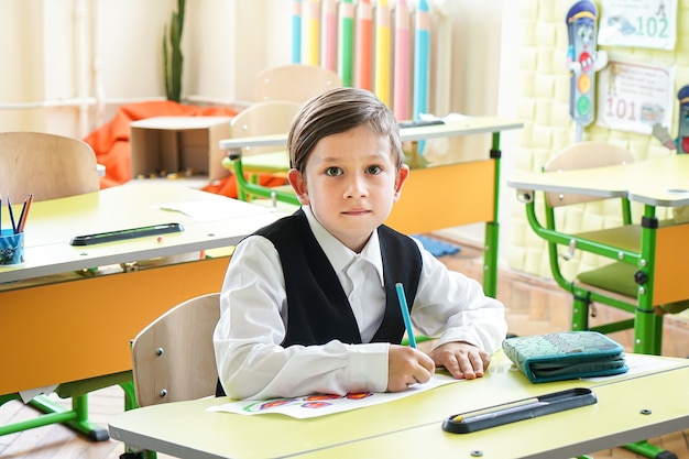 Niño sonriente feliz está dibujando y yendo a la escuela por primera vez. Niño con mochila y libro. Cabrito en el interior de la sala de clase con pizarra sobre un fondo. De vuelta a la escuela.