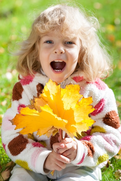 Niño sonriente feliz con hojas de arce amarillas en el parque otoño