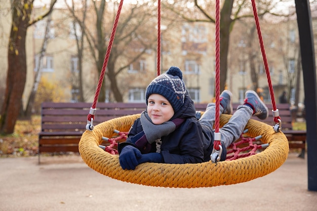 Un niño sonriente feliz monta un columpio en un parque infantil columpio cesta hamm