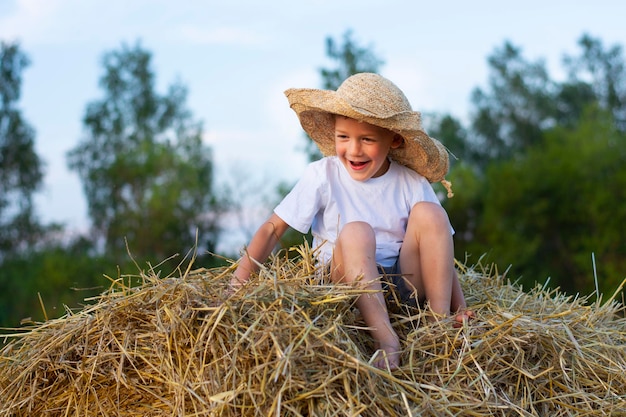 niño sonriente feliz en la pila de paja verano de agosto