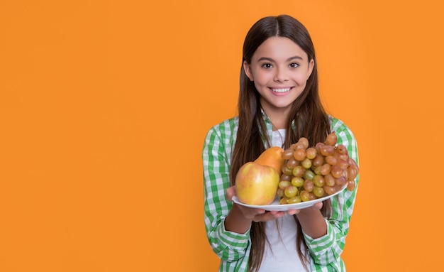 niño sonriente feliz con plato de fruta sobre fondo amarillo