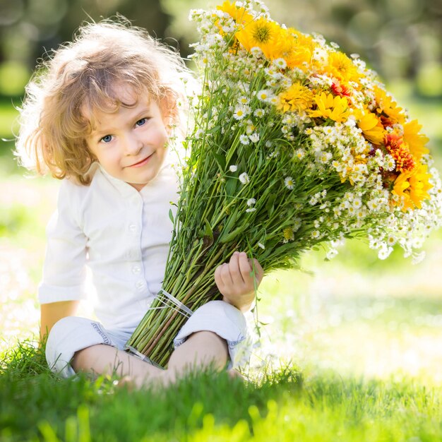 Niño sonriente feliz con ramo de flores de primavera sentado en la hierba verde al aire libre