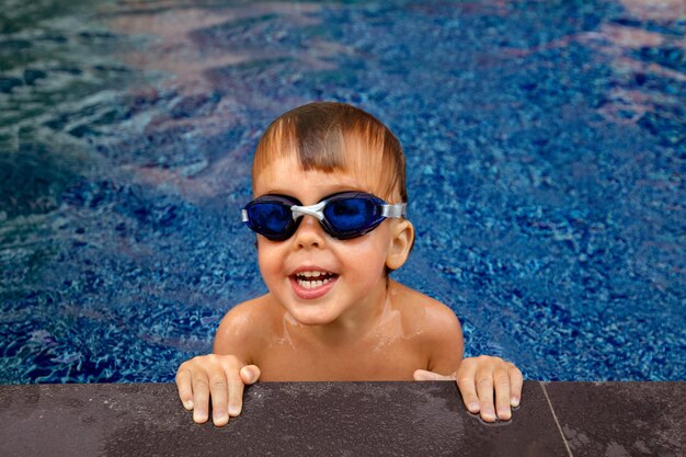 Niño sonriente en gafas en el agua cerca del borde de la piscina