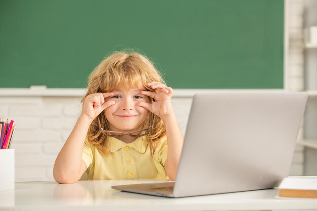 Niño sonriente con gafas estudia en línea en la clase de la escuela con la escuela de computación