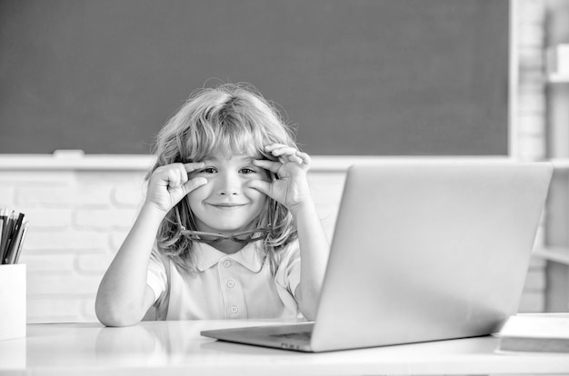 Niño sonriente con gafas estudia en línea en la clase de la escuela con la escuela de computación