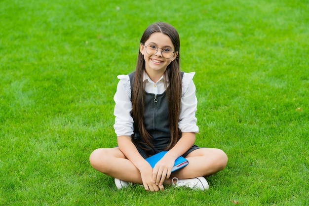 Niño sonriente con gafas sentado en la hierba verde con libro