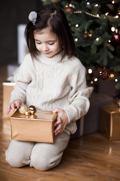Niño sonriente gir sentado bajo el árbol de Navidad con adornos
