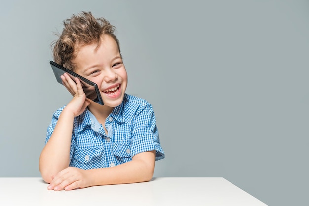 Niño sonriente hablando por teléfono mientras está sentado en la mesa sobre un fondo rosado