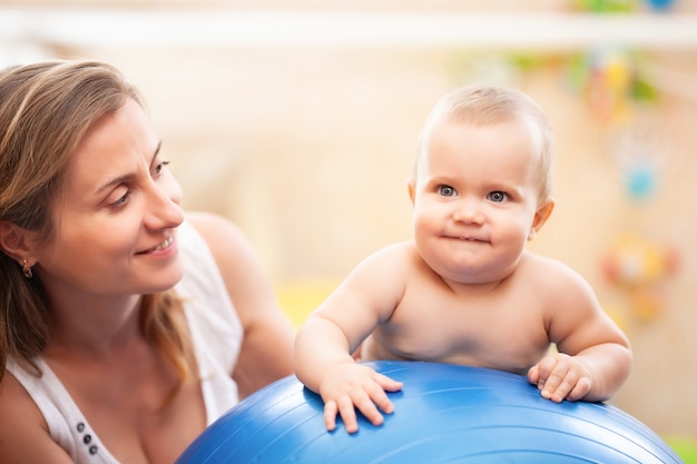 Niño sonriente haciendo ejercicio en la gran bola azul de fitness con la madre