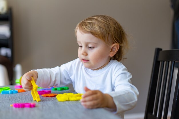 Niño sonriente moldes de plastilina de colores en la mesa