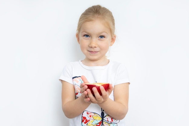 Niño sonriente niña rubia sosteniendo media manzana sobre un fondo blanco.