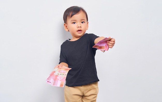 Niño sonriente niño de 2 años con camiseta negra dando billetes de rupias indonesias aislados de fondo blanco