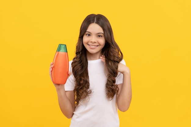 Niño sonriente con el pelo largo mantenga la botella de champú, anuncio.