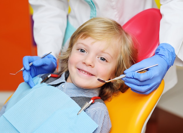 Niño sonriente con el pelo rizado claro en el examen en la silla dental