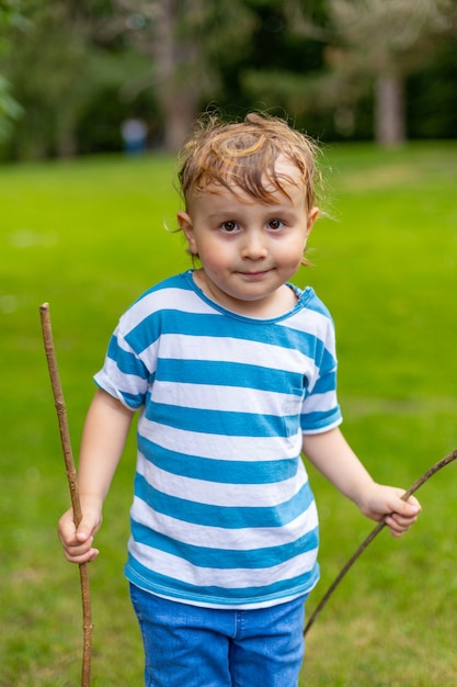 Niño sonriente con pelos sudorosos sosteniendo palos de madera y jugando en el parque en verano