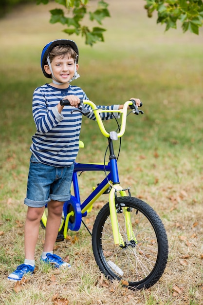 Niño sonriente de pie con bicicleta en el parque