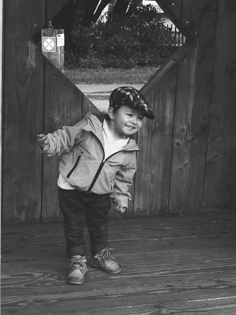 Foto niño sonriente de pie contra una estructura de madera