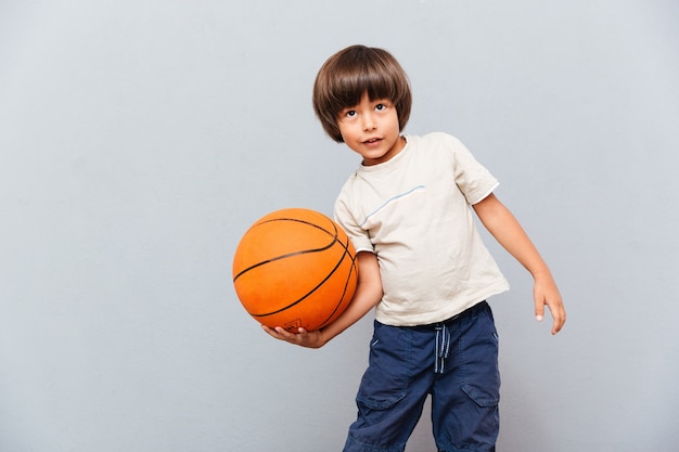 Niño sonriente de pie y jugando con pelota de baloncesto