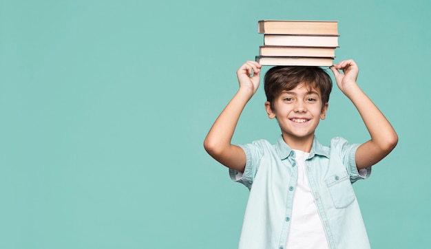 Niño sonriente con pila de libros en la cabeza.