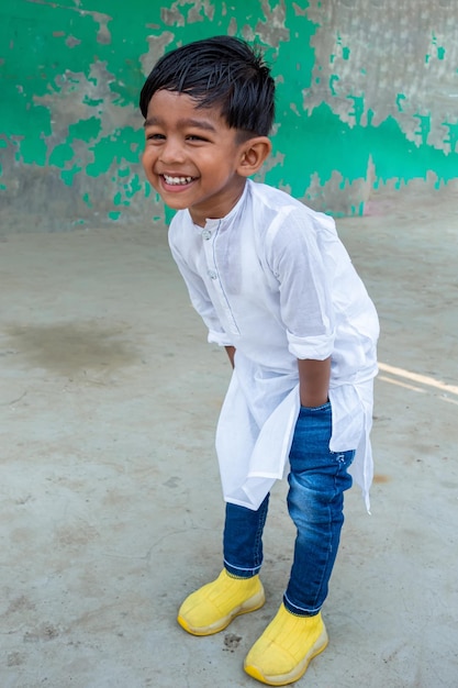 Un niño sonriente posa para una foto con panyabí blanco y jeans azules con un zapato amarillo.