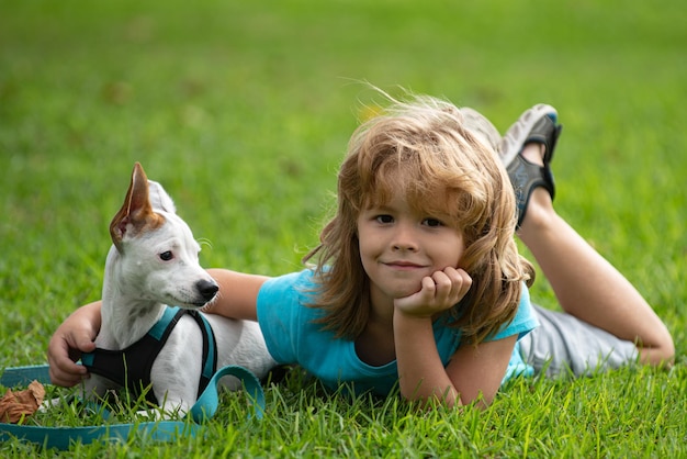 Niño sonriente sentado en el césped con divertido perrito niño feliz jugando con perro en césped