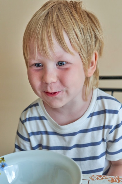 Niño sonriente se sienta delante de un plato limpio vacío