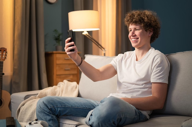 Un niño sonriente se sienta en el sofá de la sala con su teléfono por la noche